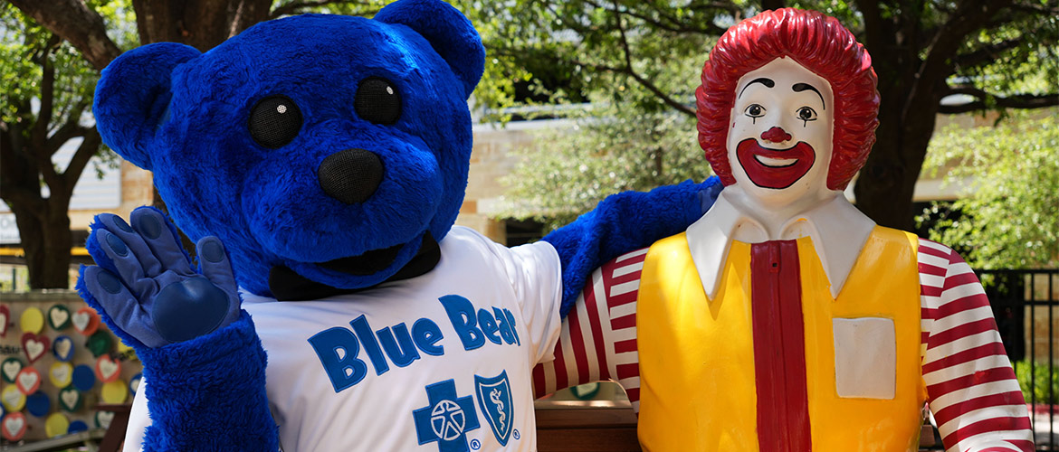 Blue Bear and Ronald McDonal sit on a bench celebrating new virtual library